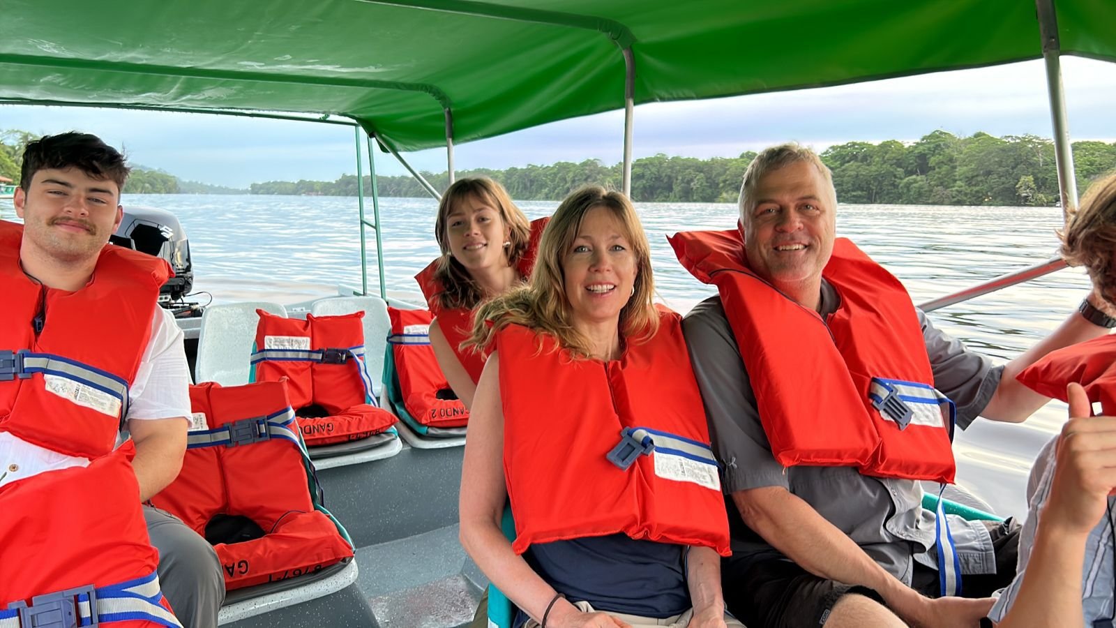 Familia sonriente disfrutando de un tour privado en bote por los canales de Tortuguero con chalecos salvavidas.